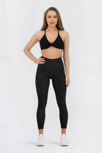 Woman wearing a black sports bra and leggings with white polka dots on a white background