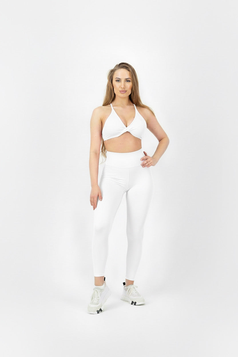 Woman wearing a white sports bra and leggings on a white background